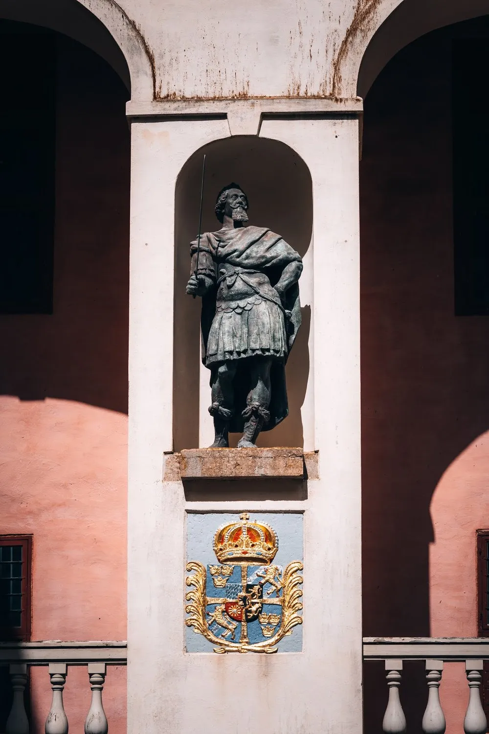 Statue eines bärtigen Mannes mit Speer in einer weissen Wandnische, darunter ein Wappen mit goldener Krone