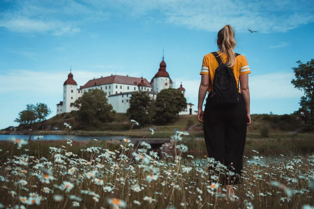 Frau in gelbem Shirt und mit Rucksack steht in der Margeritenwiese und blickt auf das Schloss