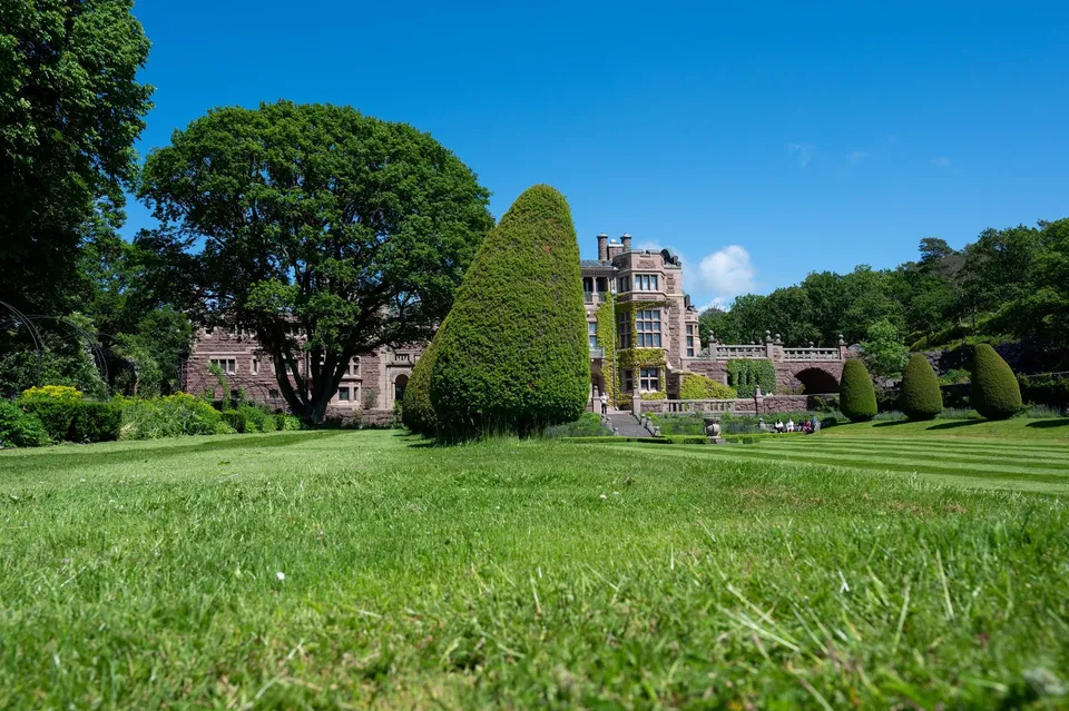 Das Schloss Tjolöholm hinter einer gemähten Wiese und einem kegelförmig geschnittenen Baum