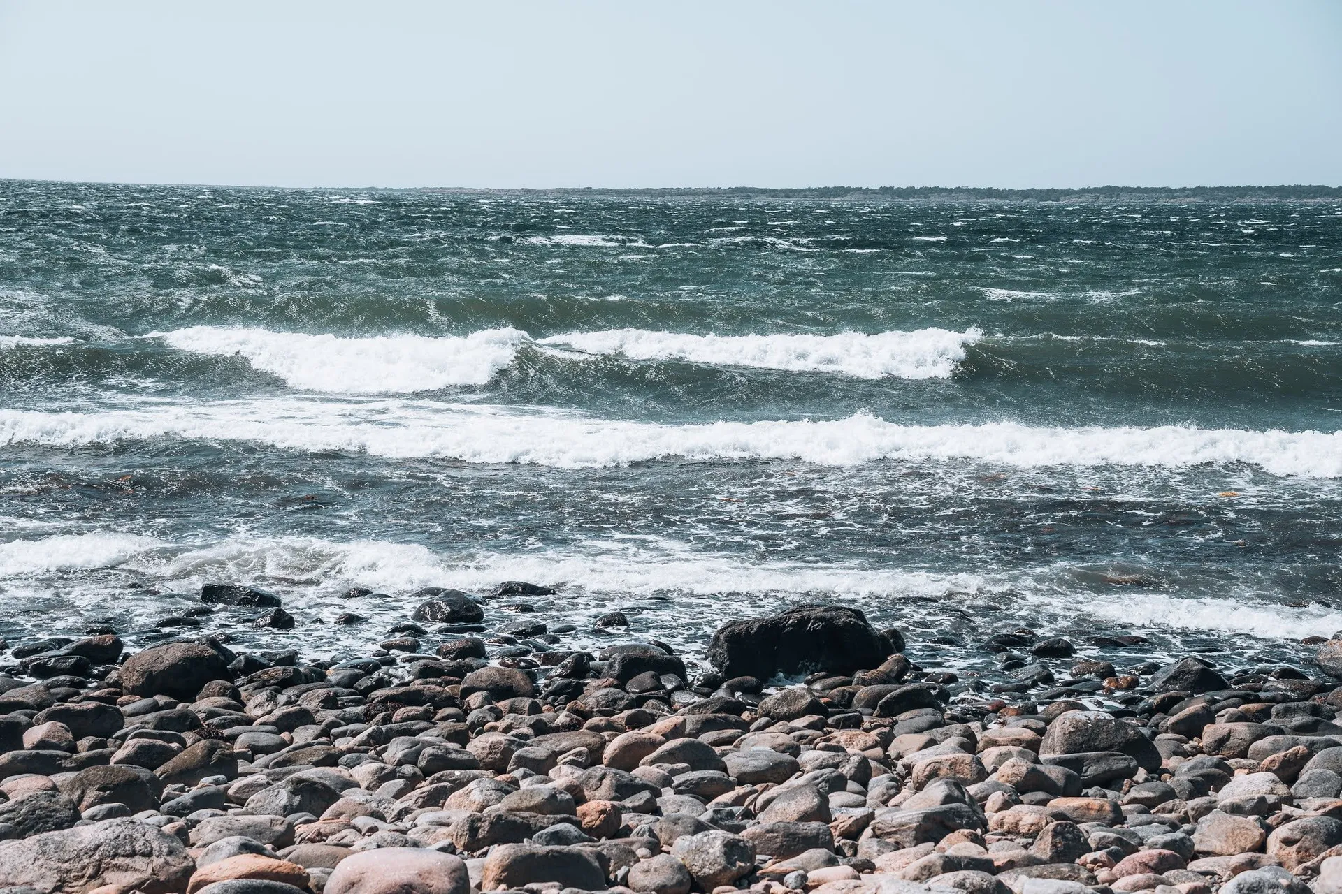 Waves with white crests roll onto a beach of round stones