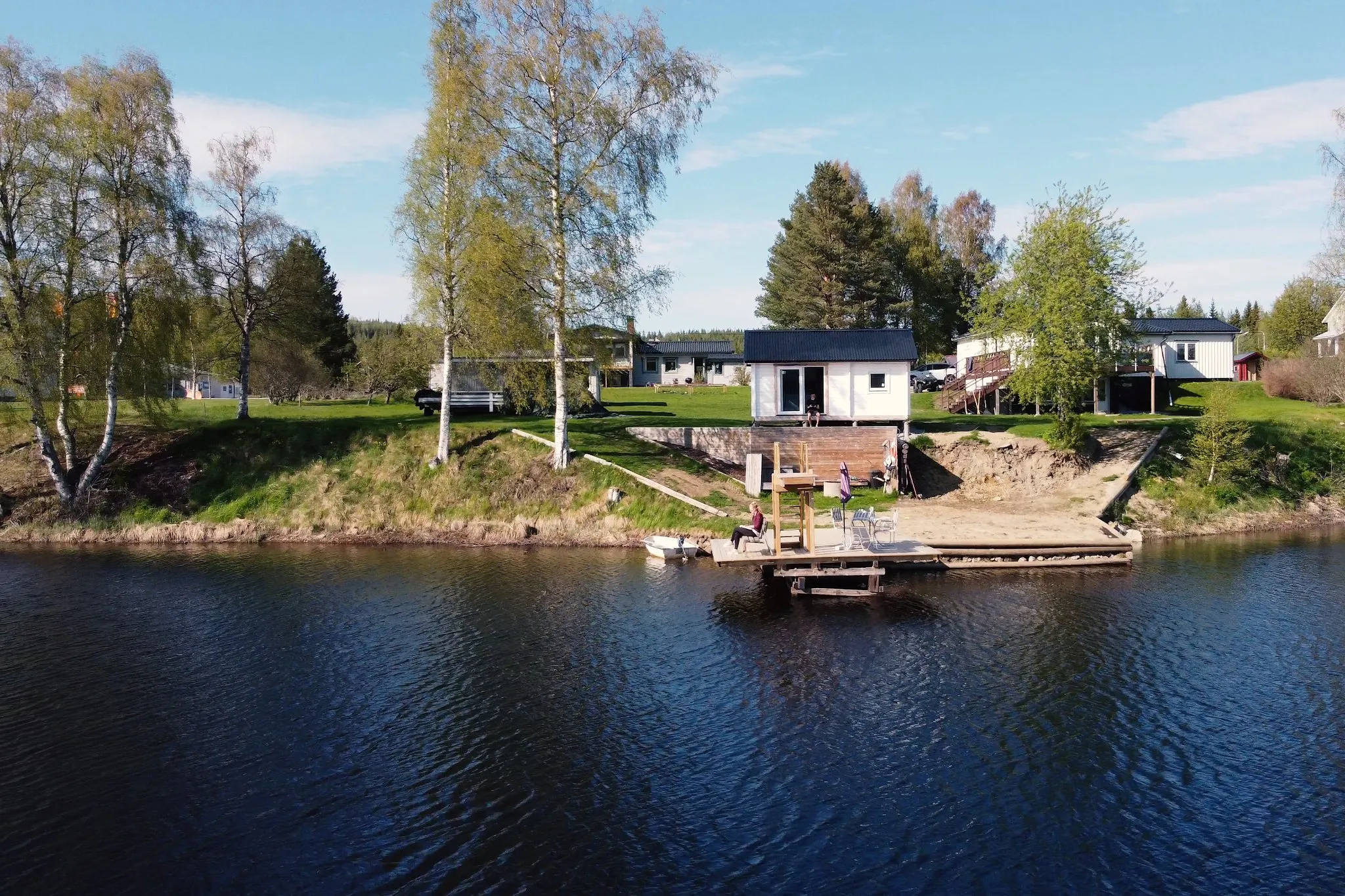 View across the dark lake to a white house and a wooden jetty with a person sitting on it