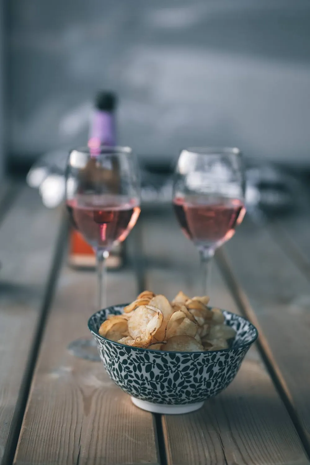 Two glasses of rosé and a bowl of chips on a wooden table