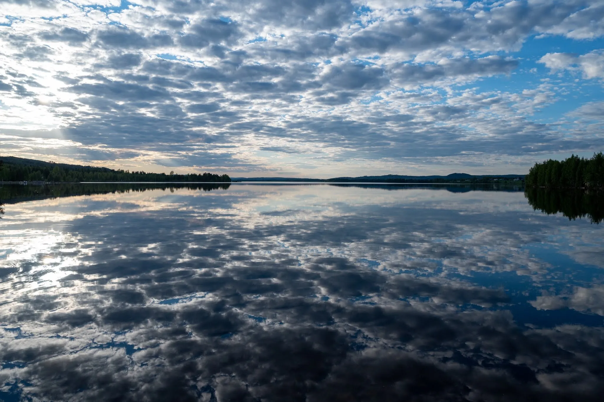 Clouds reflected in a calm lake, wooded shores to the left and right