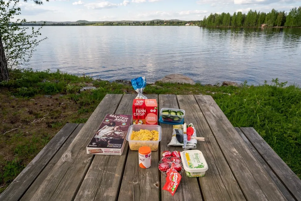 Picnic table on the lakeshore near Rätan with curry rice, crispbread, butter and a game box