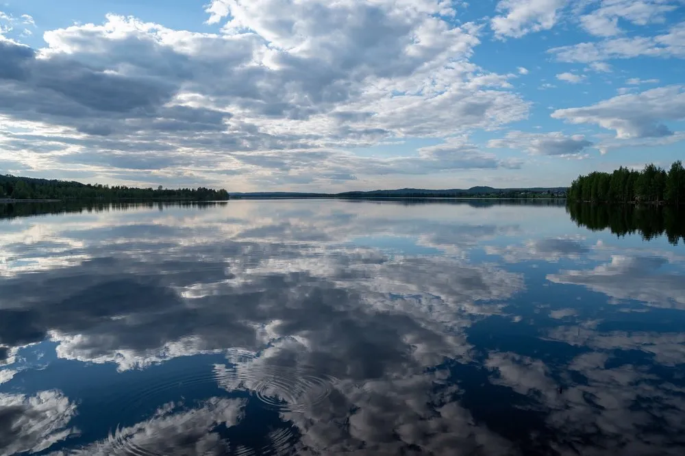 Clouds and blue sky reflected in the smooth water of the lake near Rätan