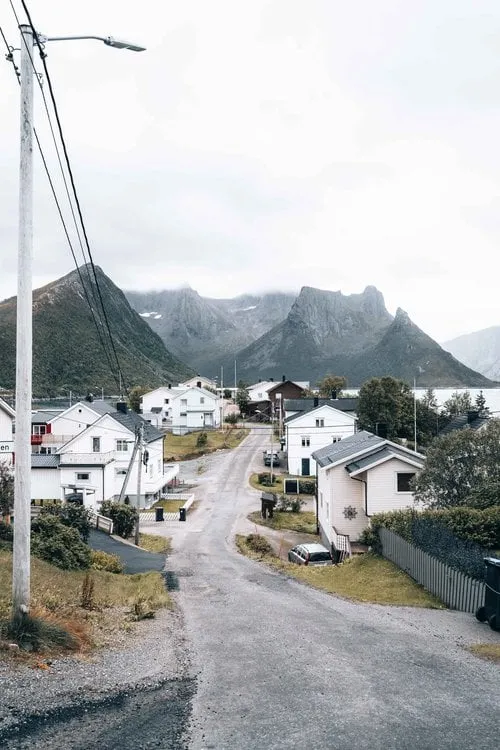 Die Dorfstrasse von Husøy zwischen weissen Häusern, dahinter spitze Berge
