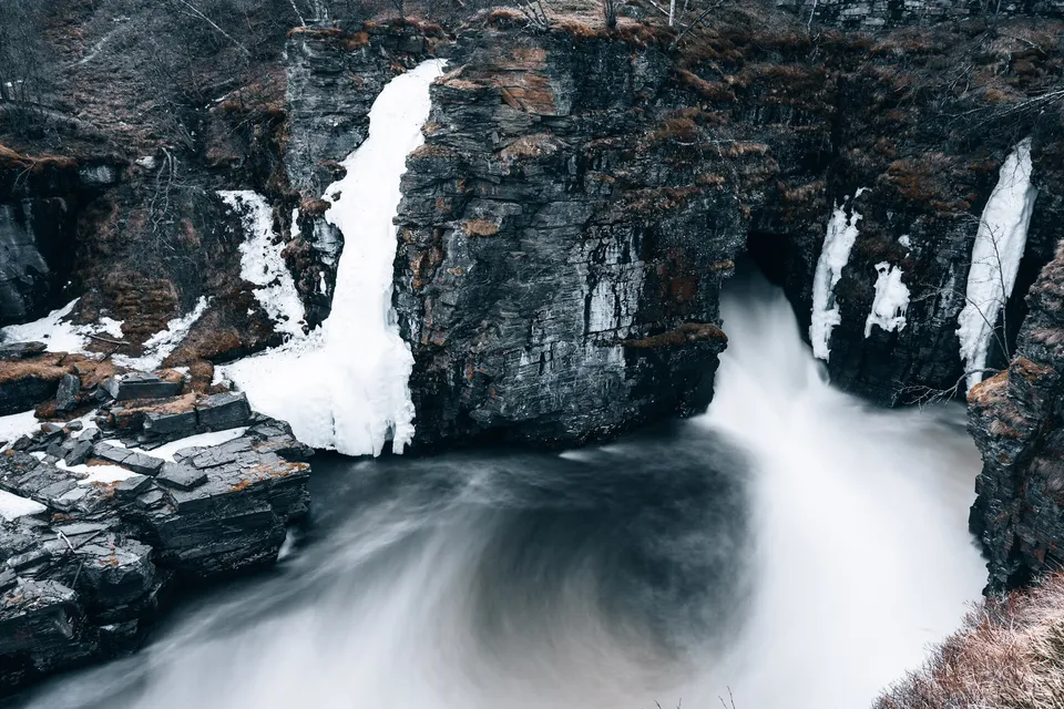 Der Wasserfall im Abisko Nationalpark stürzt zwischen dunklen Felswänden mit Eisresten in ein weiss schäumendes Becken