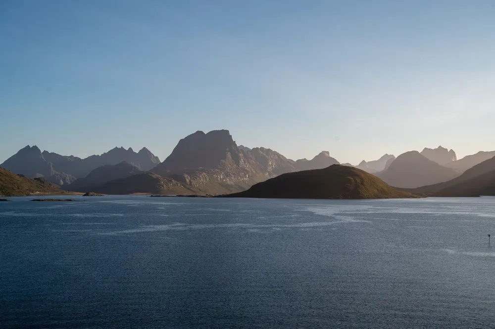 Staggered mountain ranges in the evening light above the water, a dark island in front