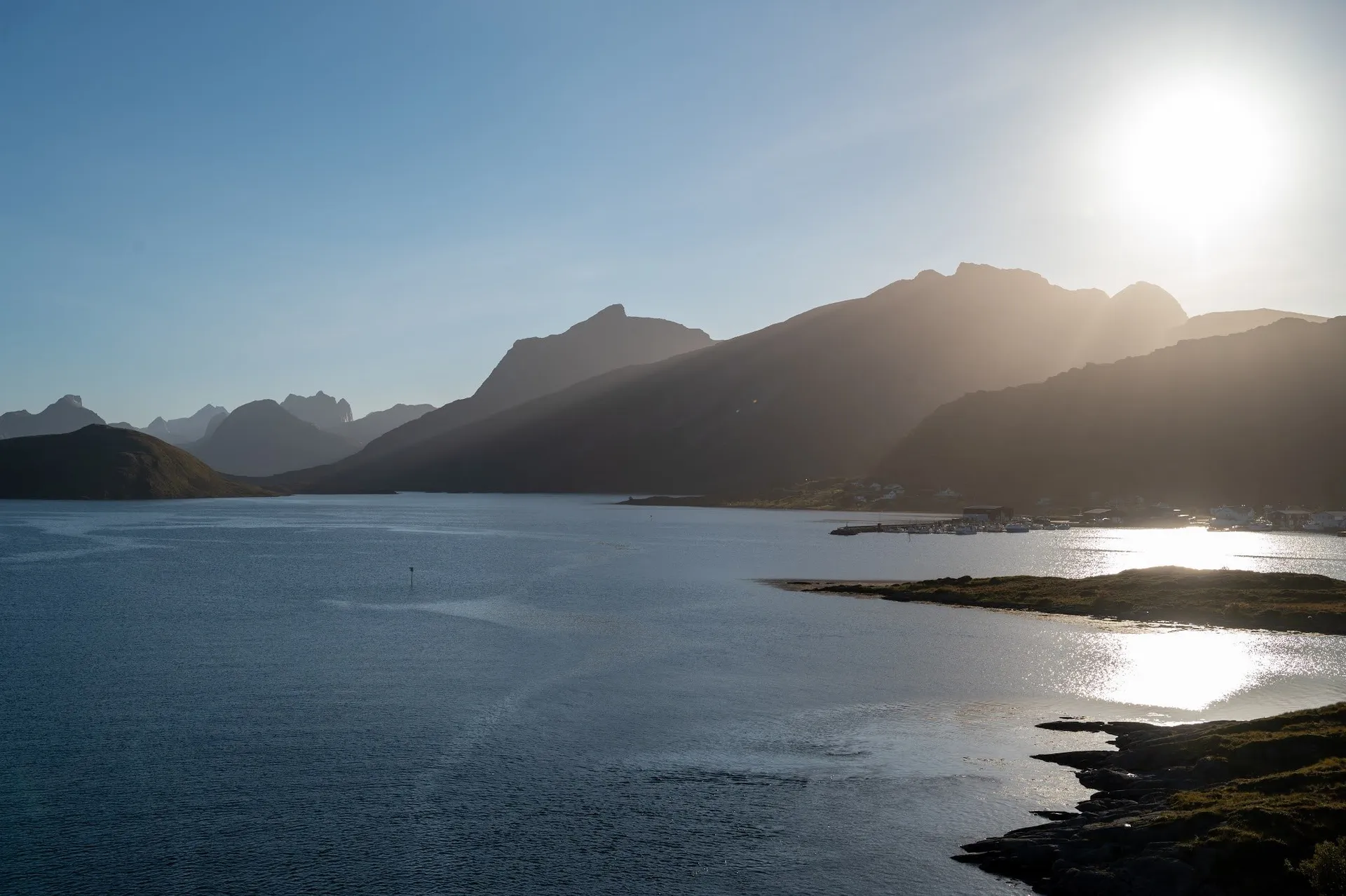 Die tief stehende Sonne über den Bergen, im Wasser spiegelt sich das Licht, am Ufer stehen Häuser