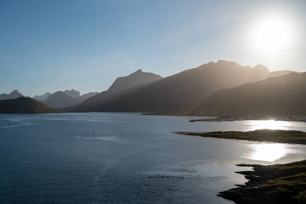 The low sun above the mountains, the light reflected in the water, houses on the shore