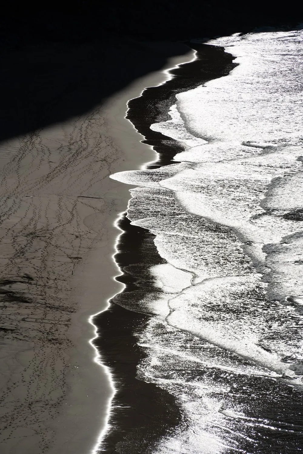 From above: the edge of the waves between dark sand and white foam, fine tracks in the sand