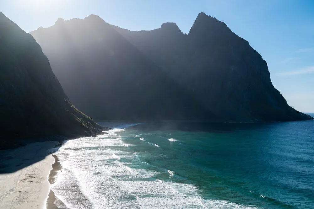 Backlight over steep rock walls, turquoise water and surf in front