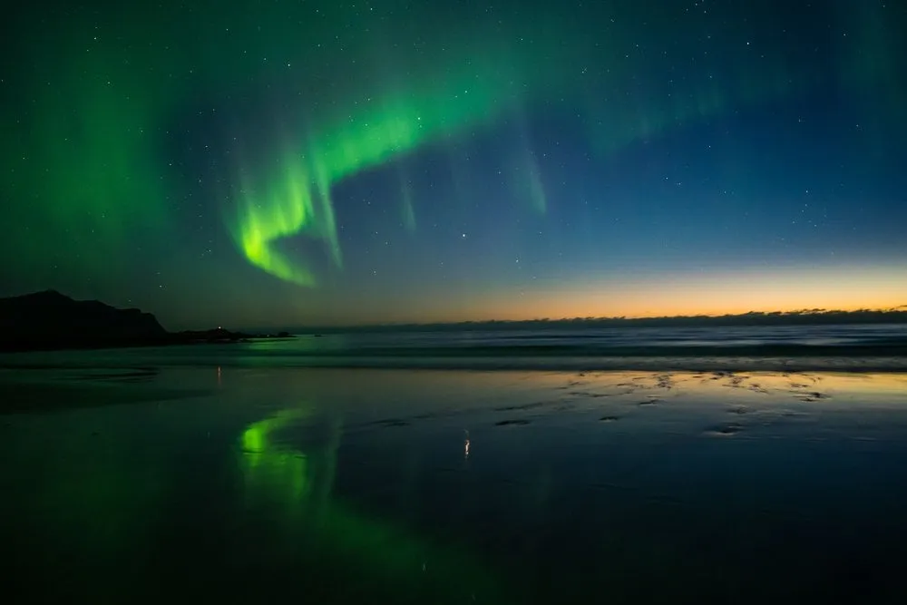 Grüne Strahlen über dem Horizont, im Sand die Spiegelung