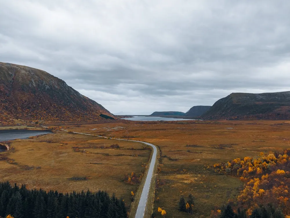 A road through a wide, autumn brown plain between two mountains, from the air on the way back to Nøss