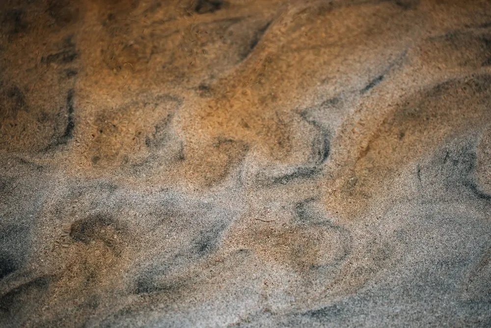 Rust brown and dark swirling patterns in the water of the iron-rich stream on the beach at Bleik