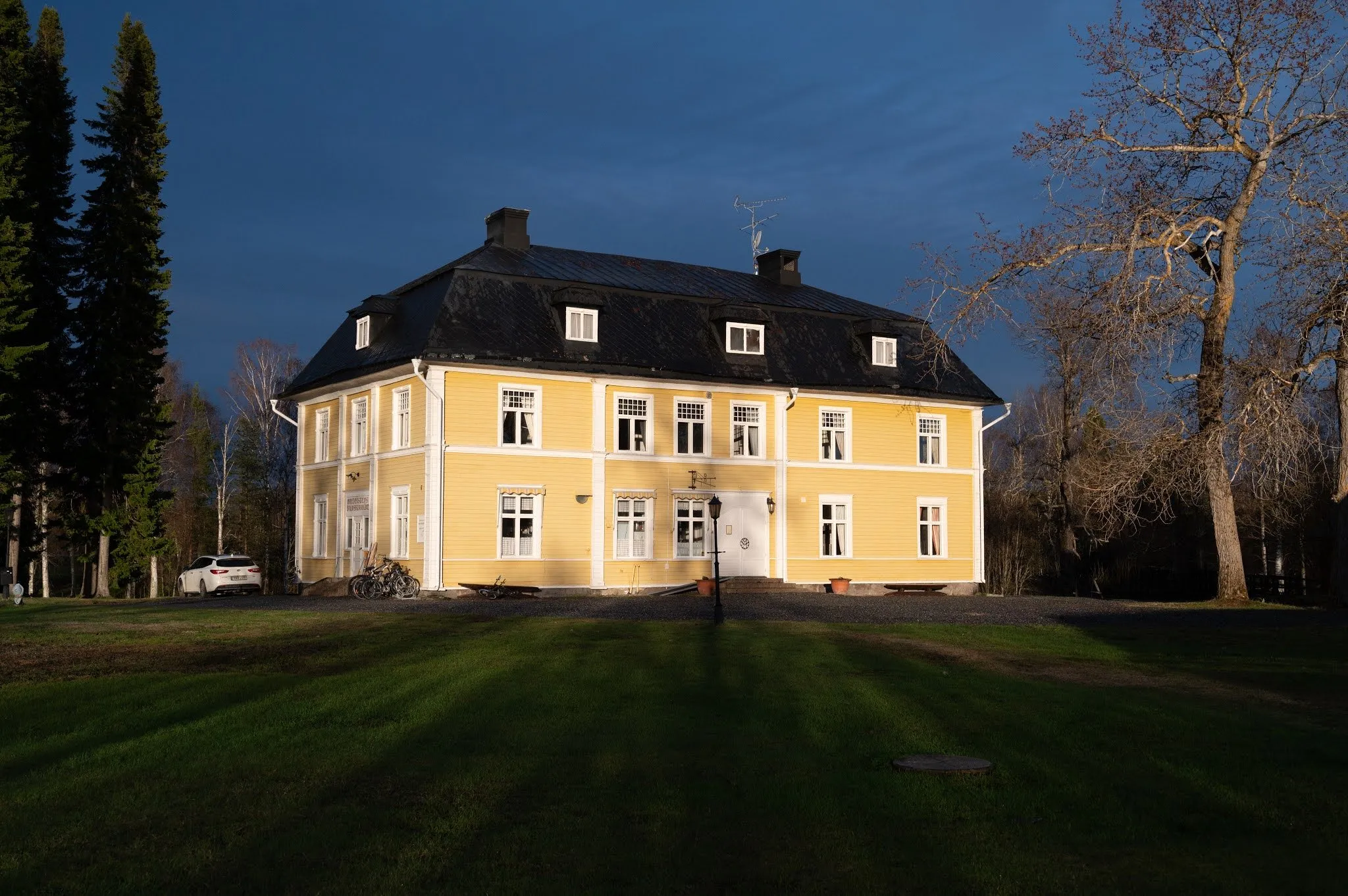 The yellow Villa Melderstein Herrgård with a dark roof in the last sunlight against a deep blue sky