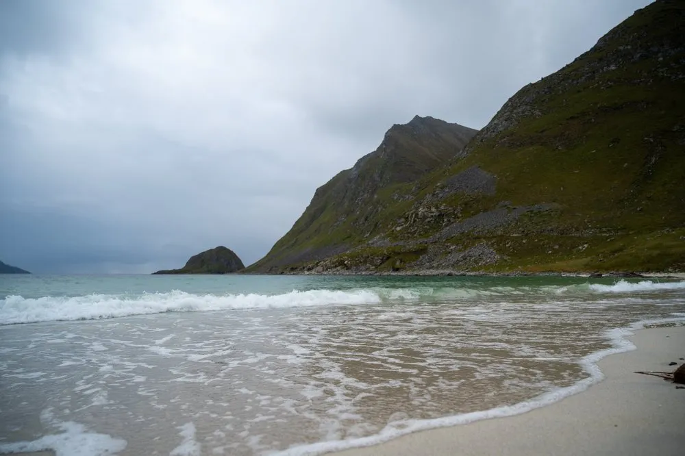 At Hauklandstranda waves run up onto the sand, a steep green mountainside rises on the right