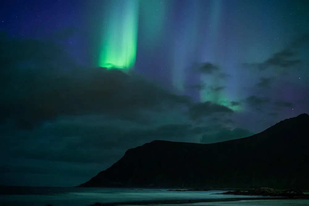 Green pillars of light above a dark mountain, the sea at the bottom edge of the picture