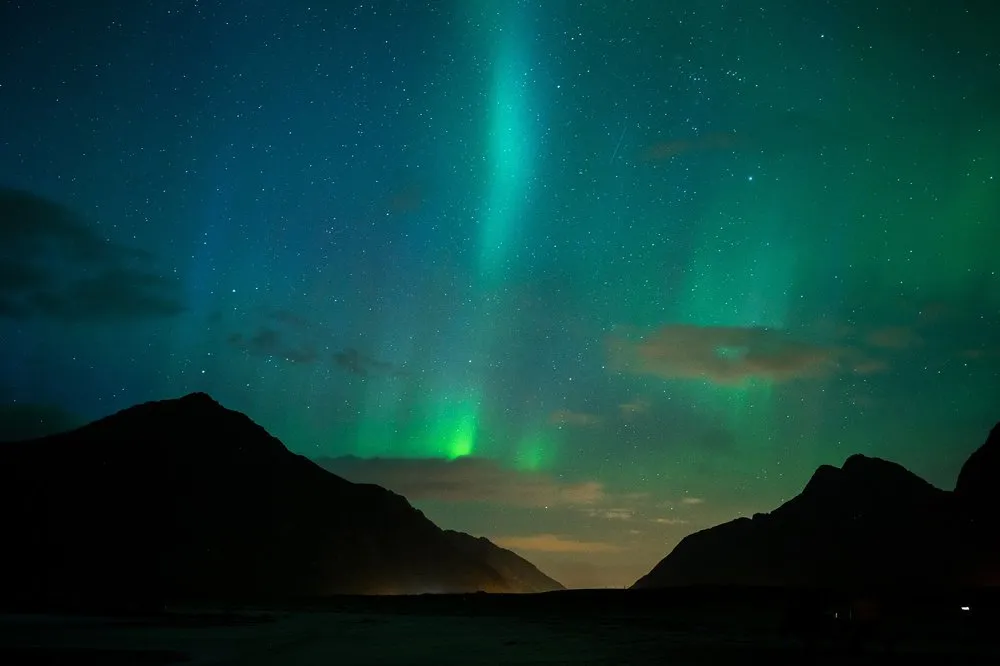 Northern lights between two dark mountain slopes, an orange glow on the horizon
