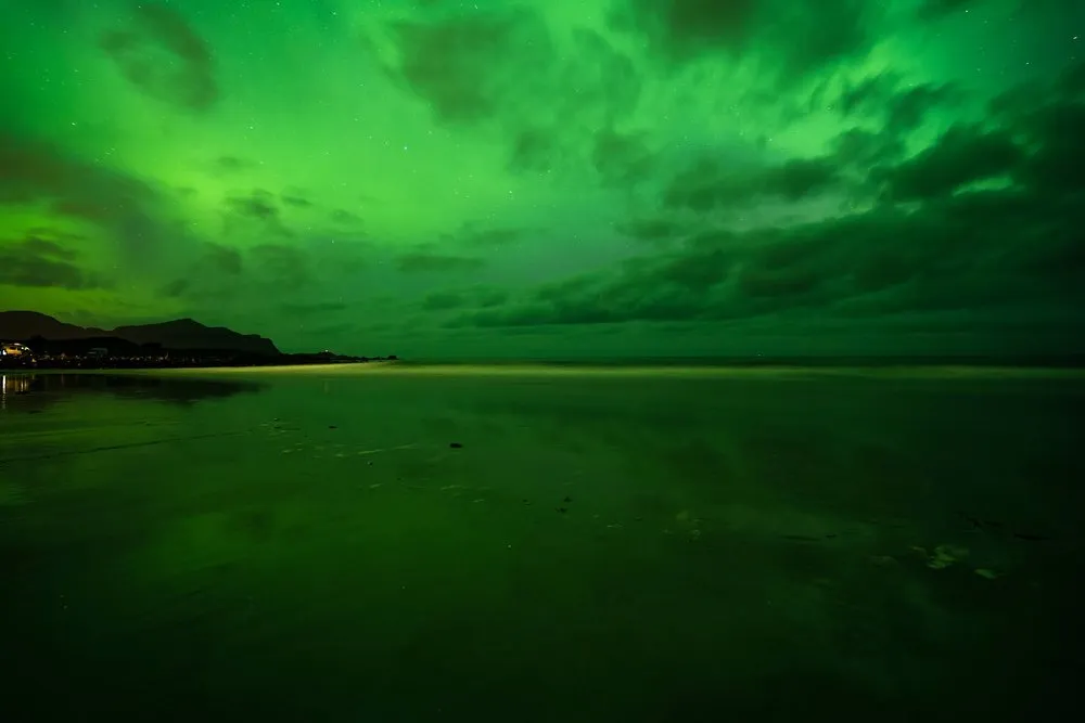 The whole sky glows green, below it a wet sandy beach reflecting the light