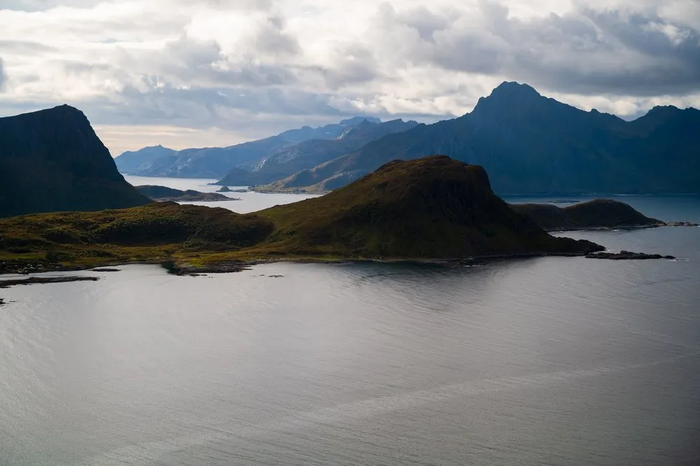 A green peninsula with staggered mountains behind it above the calm sea
