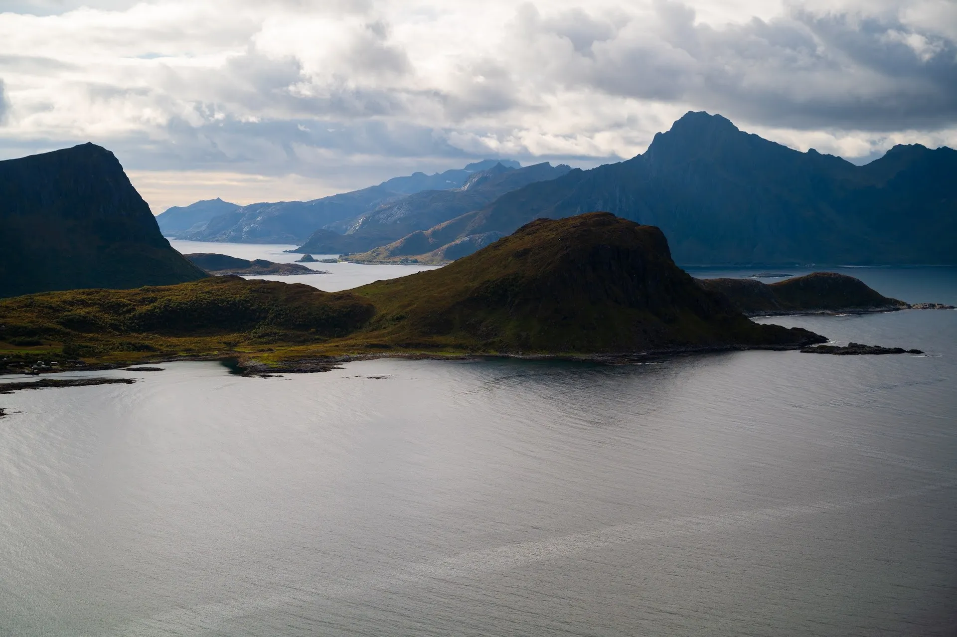 Eine grüne Halbinsel und dahinter gestaffelte Berge über dem ruhigen Meer