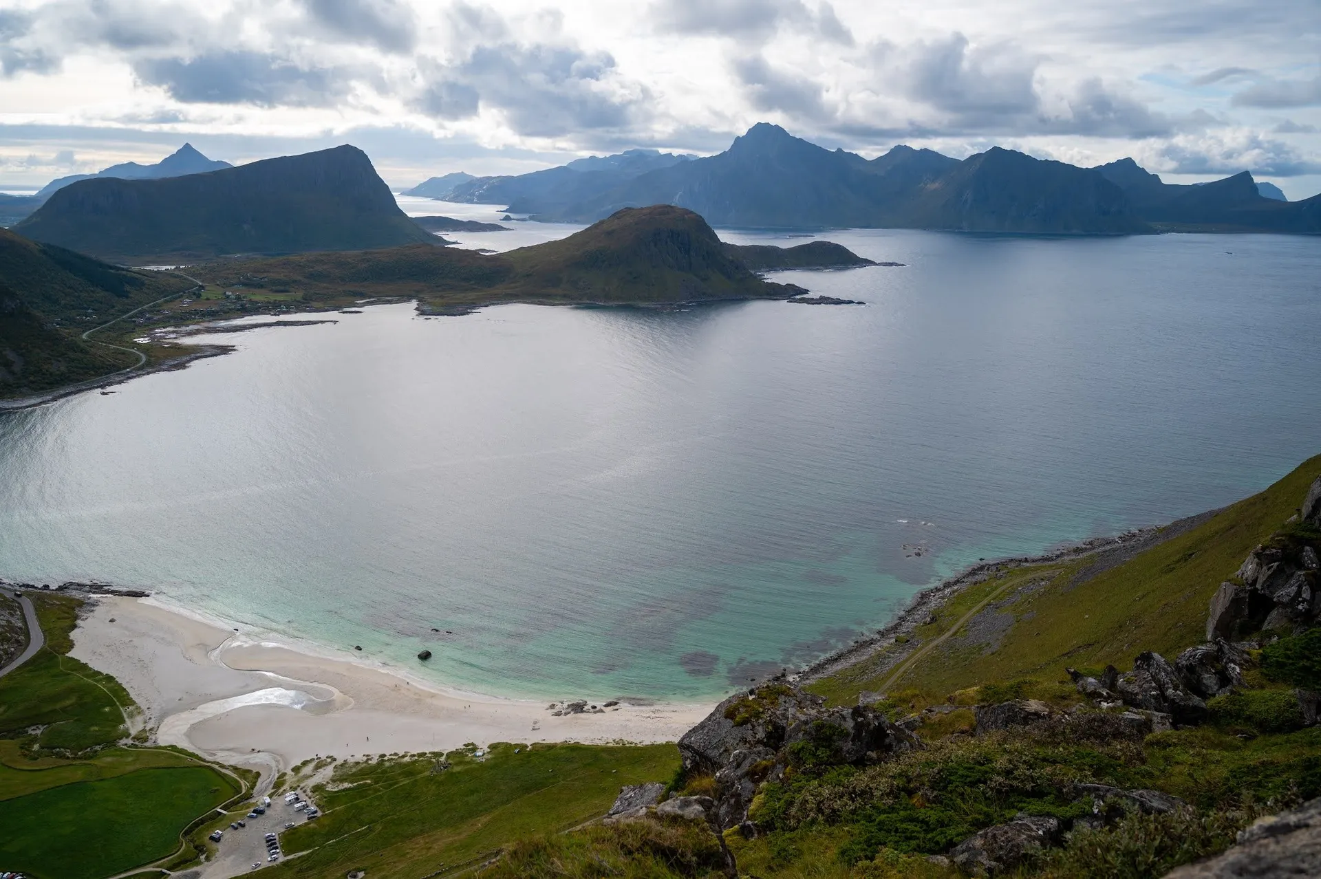Die Bucht mit türkisem Wasser und hellem Sandstrand, am unteren Rand der Parkplatz