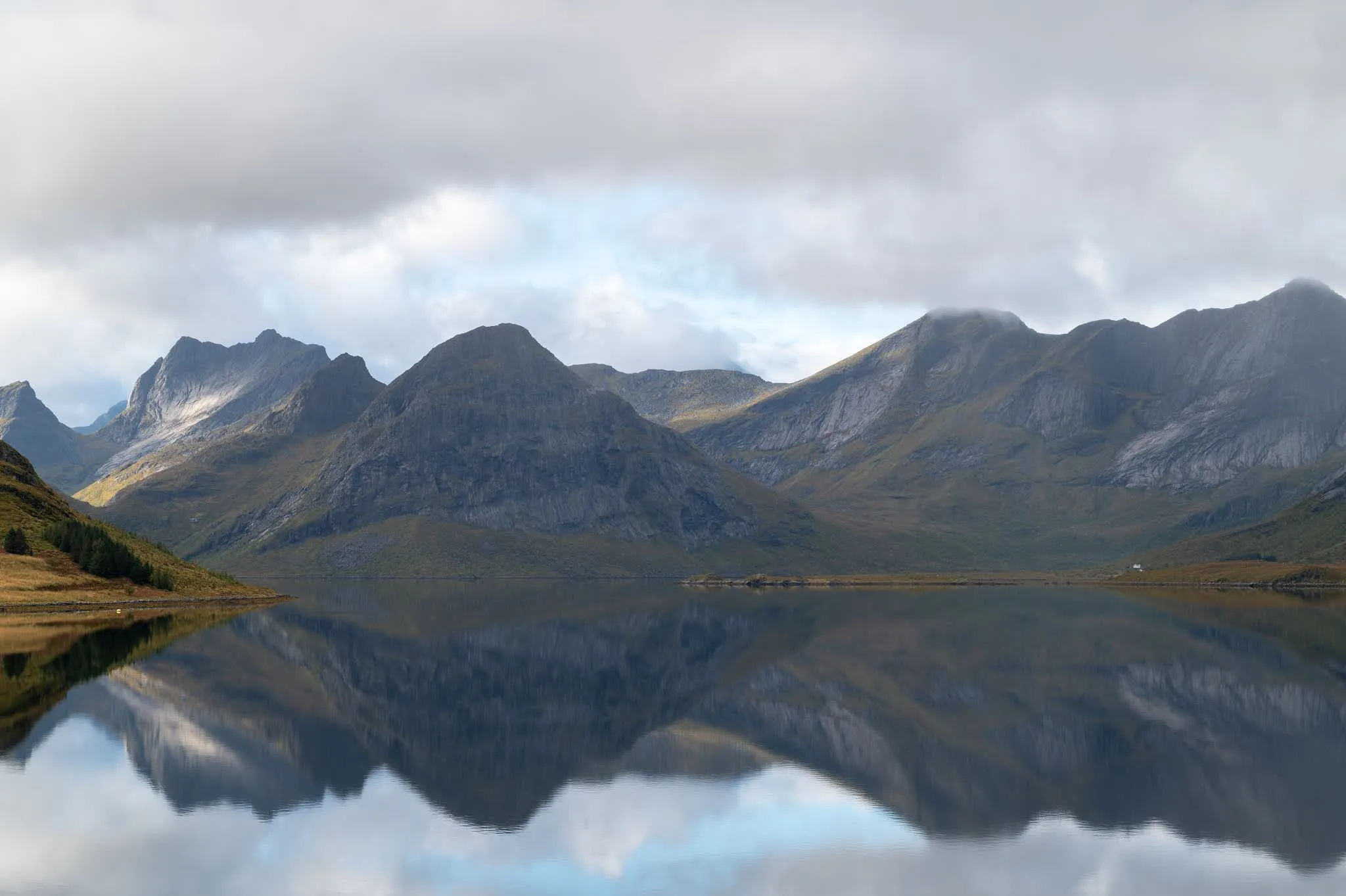 A mountain range reflected in mirror-smooth water, with clouds and blue gaps above