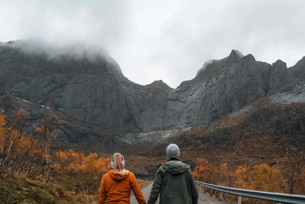Wir beide Hand in Hand auf der Strasse nach Nusfjord, vor uns die grauen Felswände in den Wolken