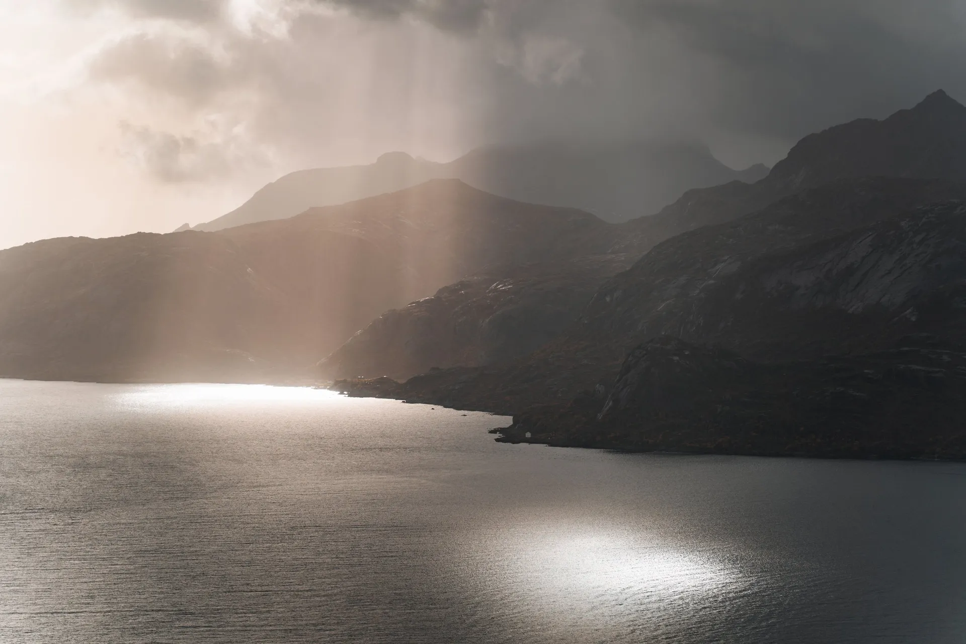 Sonnenstrahlen fallen beim Aufstieg zum Offersøykammen durch die Wolken auf das Wasser vor den dunklen Bergen