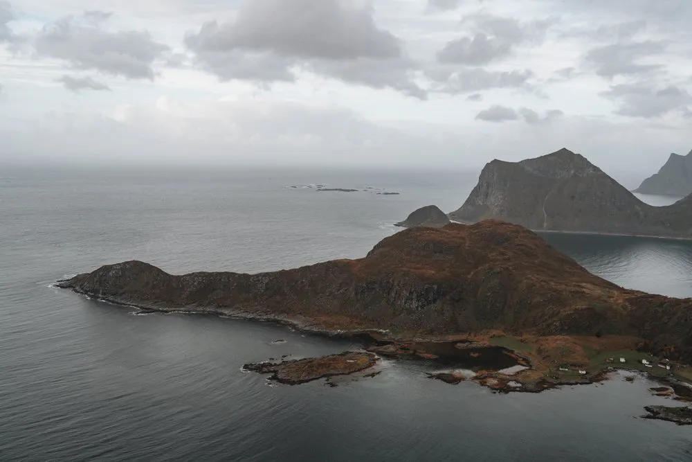 Vom Offersøykammen auf eine herbstlich rotbraune Landzunge, die sich ins graue Meer streckt, rechts ein steiler Felsberg