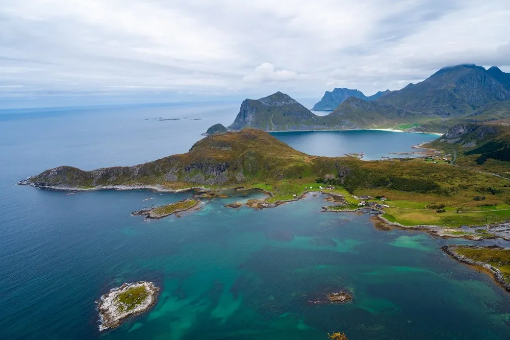 Eine grüne Halbinsel mit türkisfarbenem Wasser und dahinter Berge am Meer, von oben gesehen