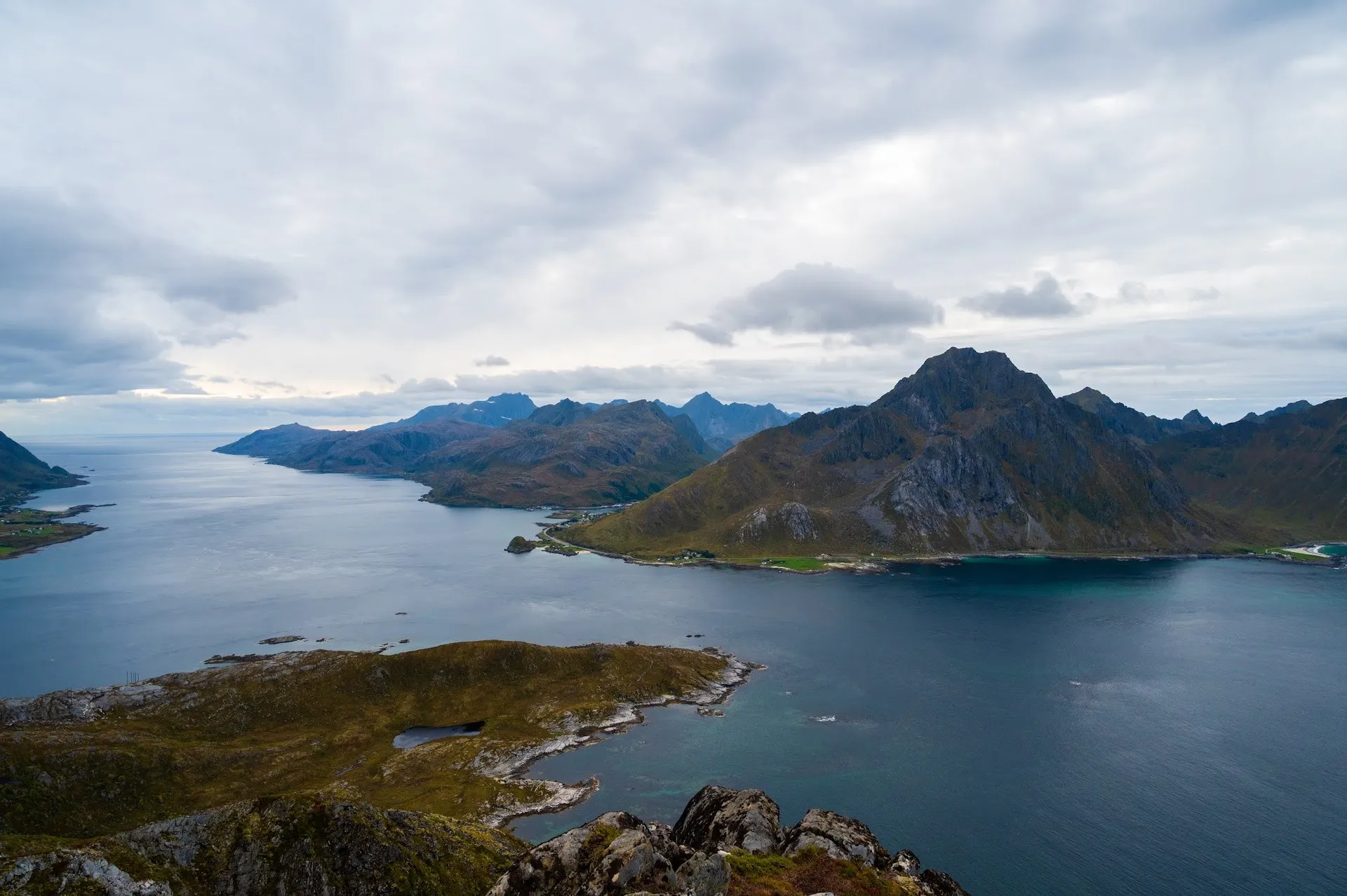 View across a dark blue fjord to a mountain massif under a cloudy sky