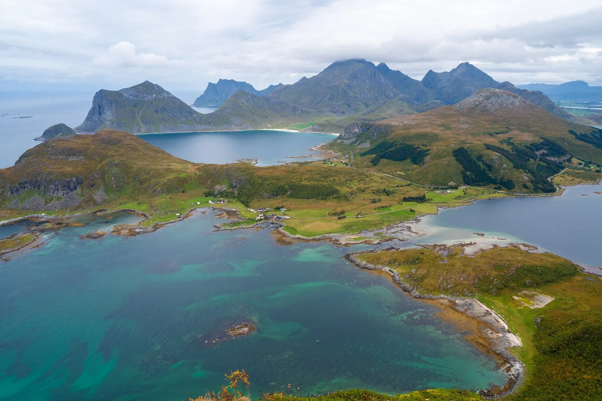 Turquoise water, a few houses on the shore and mountains with clouds on the horizon