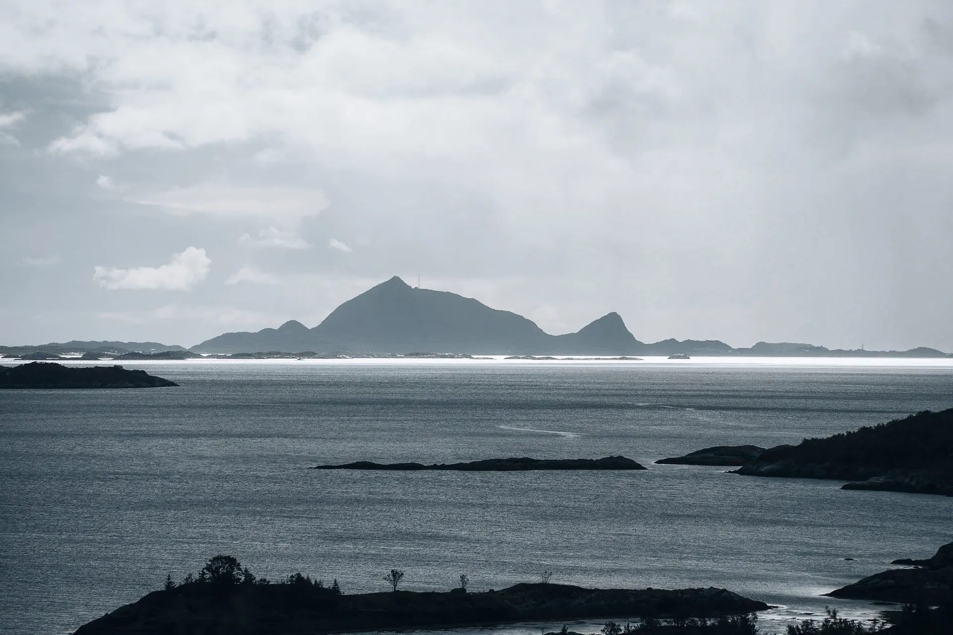 Silhouette einer bergigen Insel am Horizont über dem Meer, davor dunkle Felsinseln im Wasser