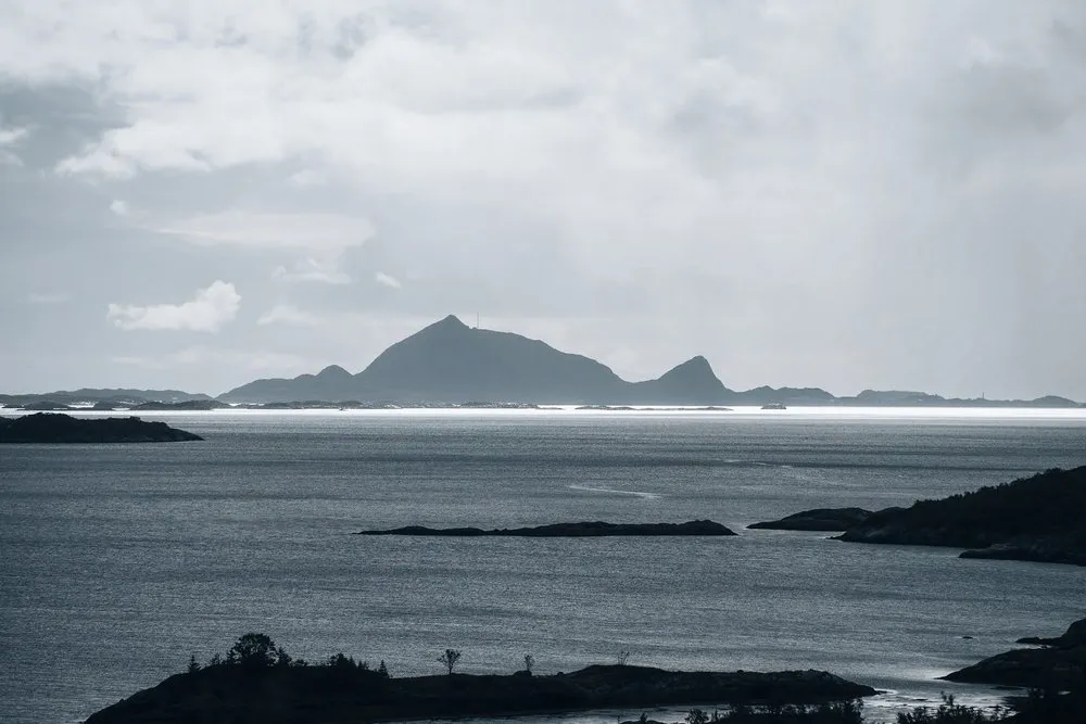 Silhouette of a mountainous island on the horizon above the sea, dark rocky islets in the water in front