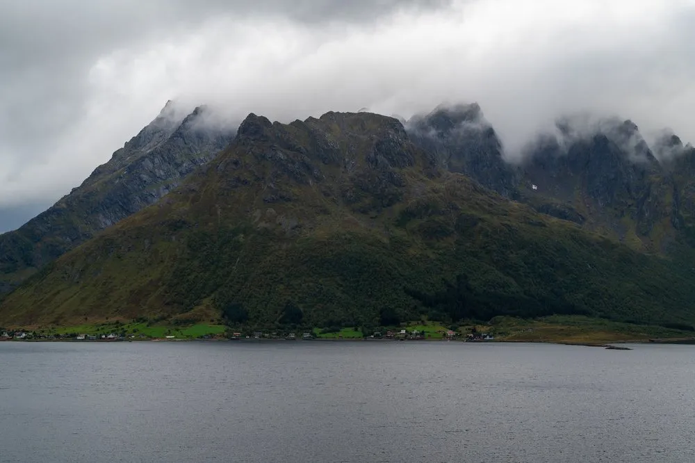 Cloud-shrouded mountain range above the water, a settlement at the foot of the slope