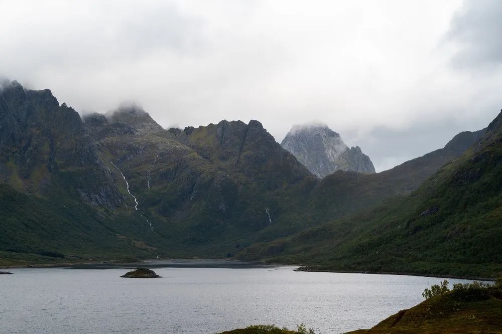 Mountains with thin waterfalls above a sea bay, a small island in the water