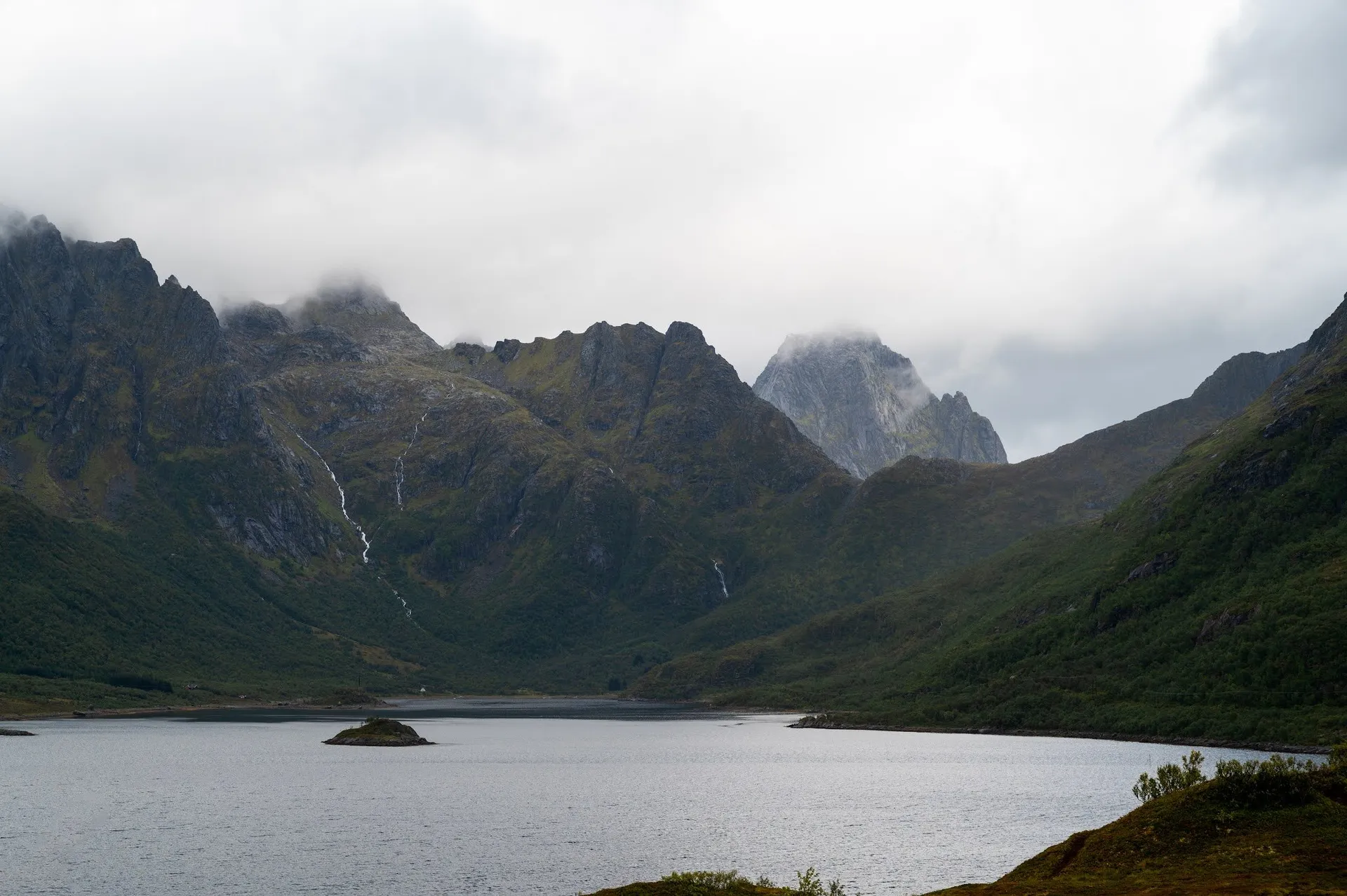 Berge mit dünnen Wasserfällen über einer Meeresbucht, im Wasser eine kleine Insel