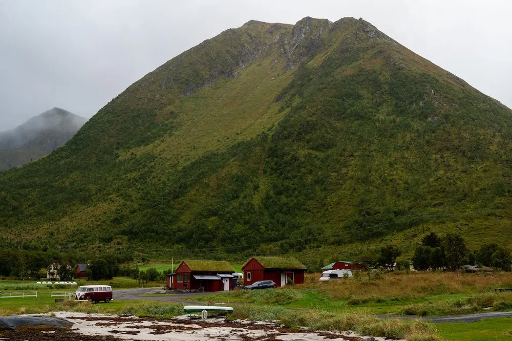 The campsite in Rystad with red houses with grass roofs at the foot of a green mountain, a VW bus on the left