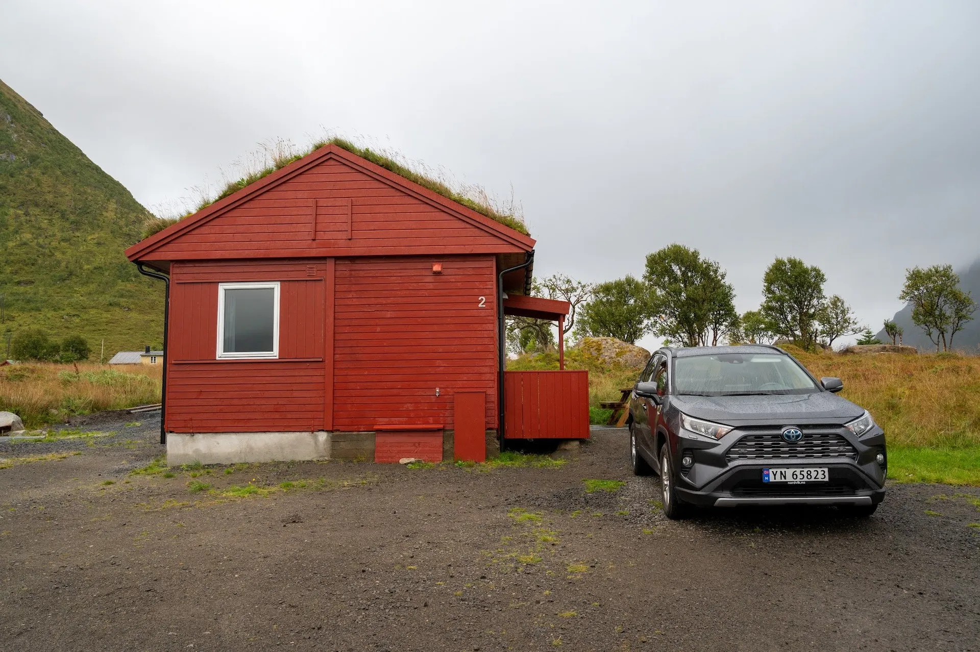 Rotes Häuschen mit Grasdach auf dem Campingplatz in Rystad, davor unser grauer Toyota RAV4