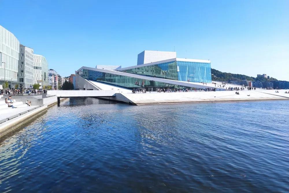 Das Opernhaus mit Glasfassade und schrägen weissen Flächen direkt am Wasser, auf den Rampen sitzen und gehen Menschen