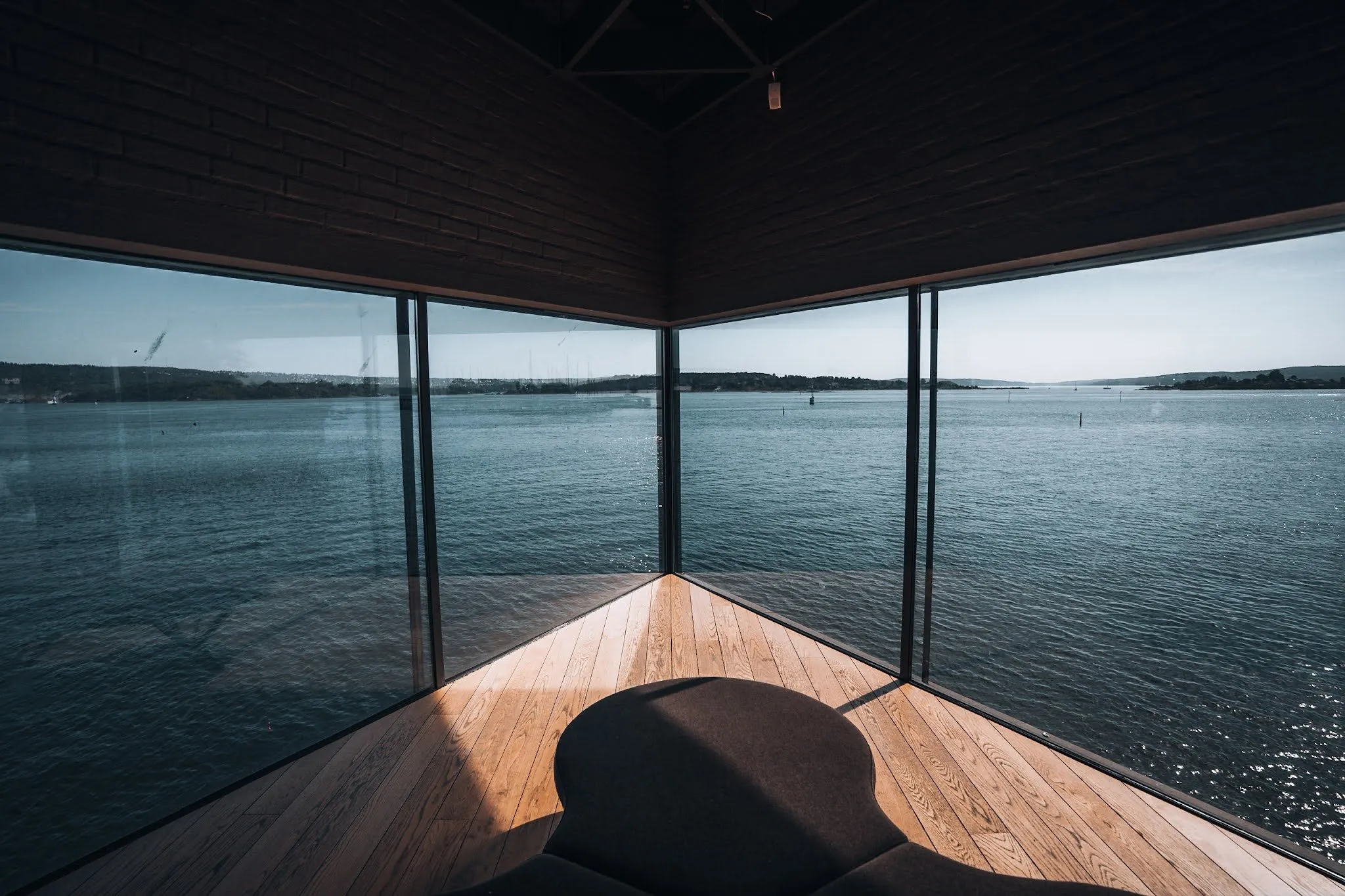 View from the corner window of the Maritim Museum over the water, in the foreground a round dark seat on a light wooden floor