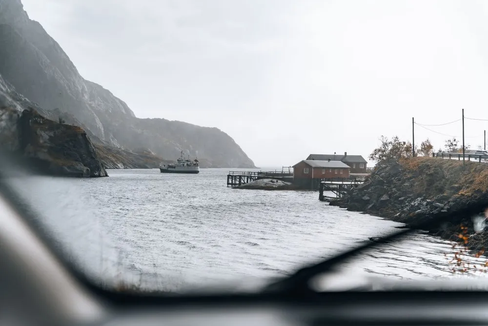 Ankunft in Nusfjord durch die nasse Windschutzscheibe, vorne der Scheibenwischer, hinten Boot und Häuser am Wasser