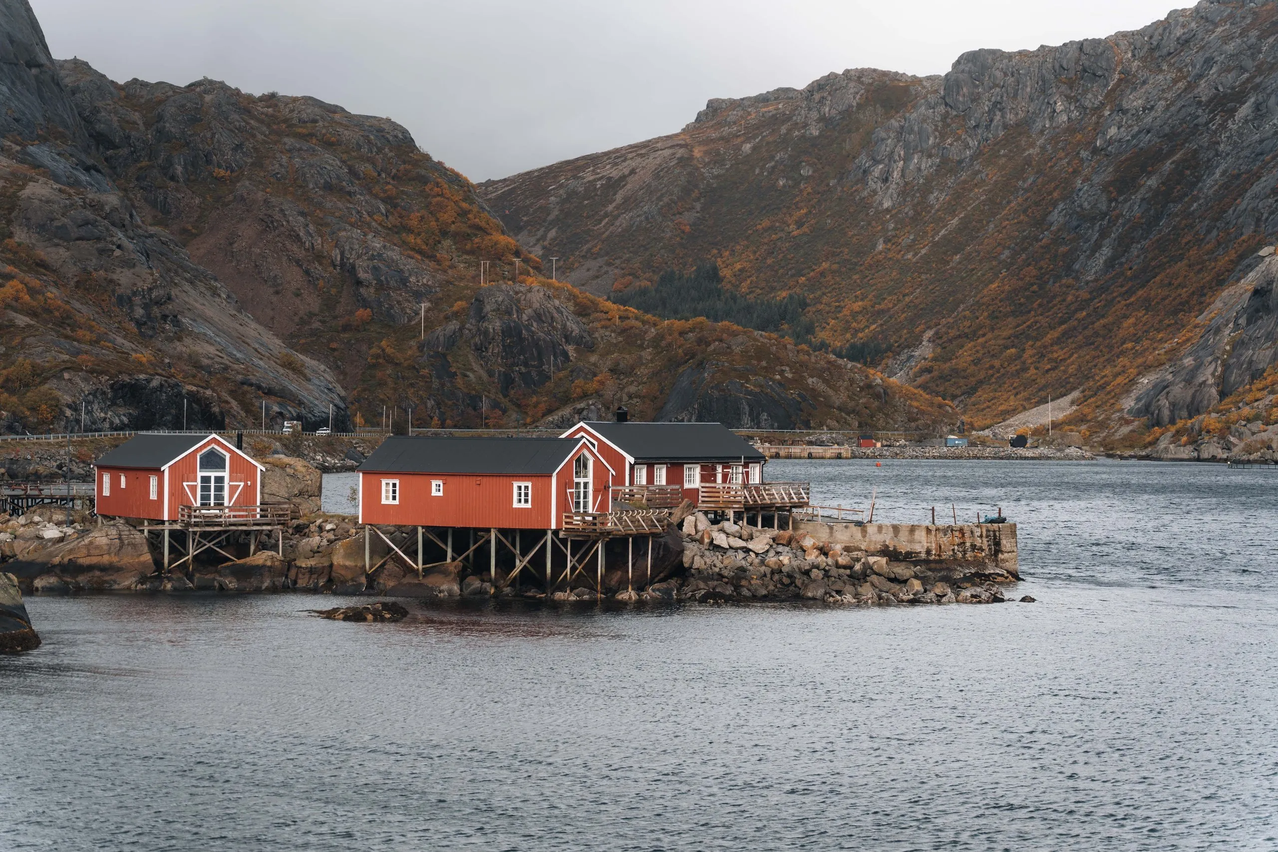 Red rorbuer on stilts on a rock in Nusfjord harbour, the mountains behind