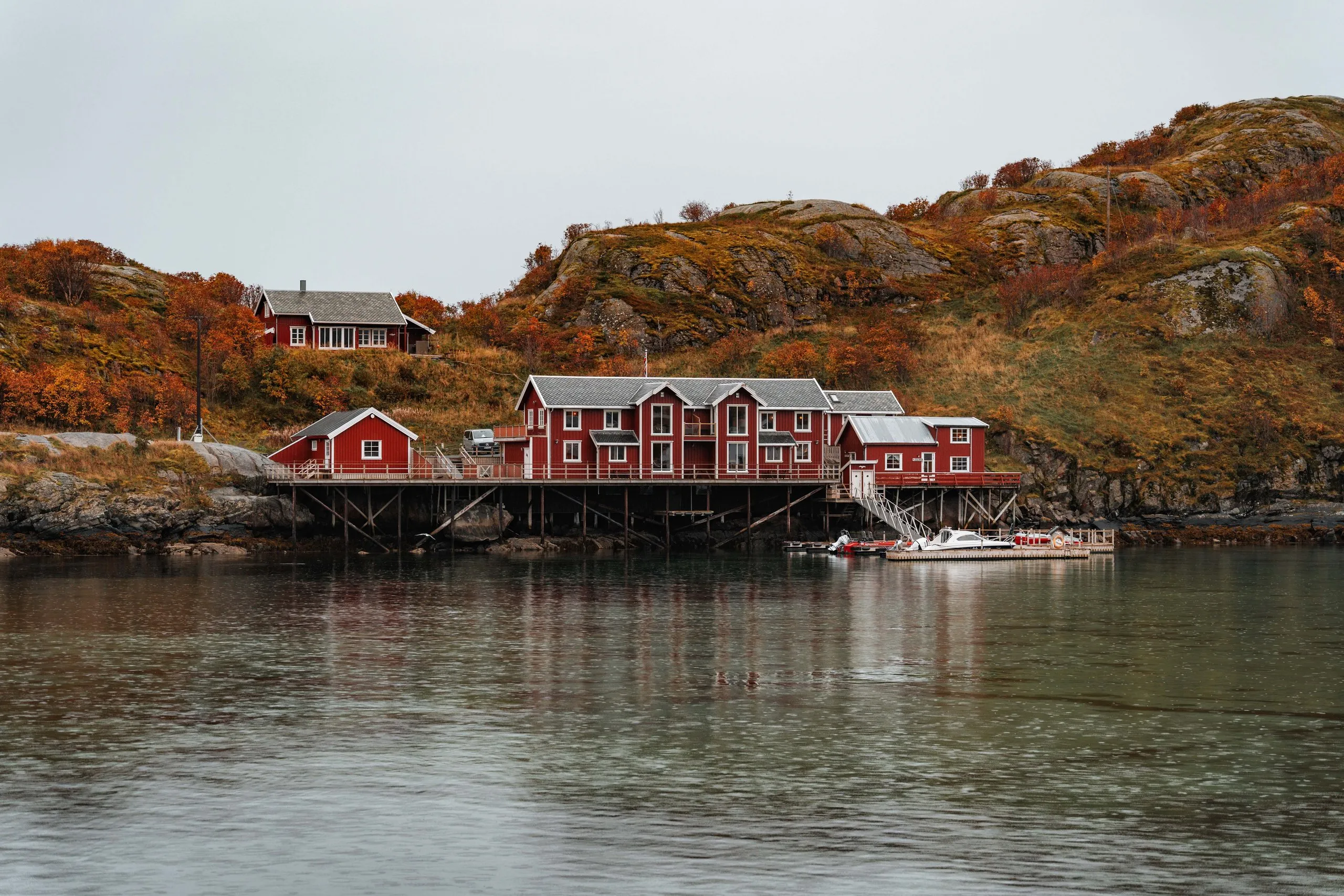 Red rorbuer on stilts above the calm water near Sakrisøy, orange autumn hills behind