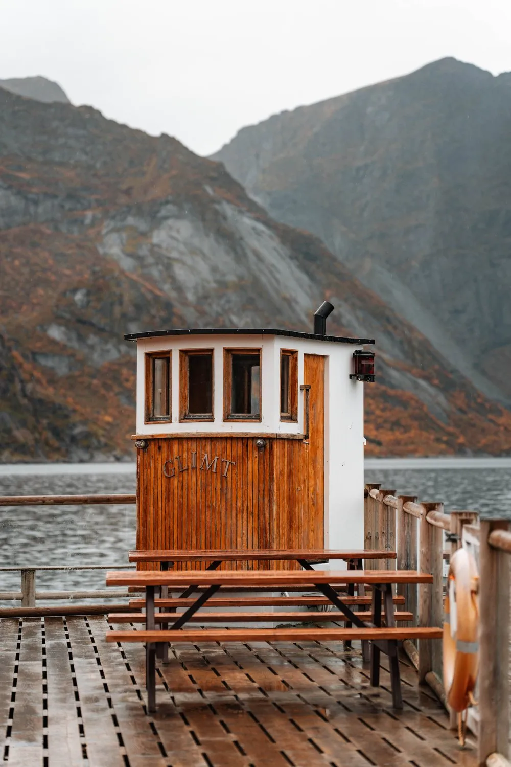 The old wooden wheelhouse of a boat on a wet wooden deck in Sakrisøy, autumn mountains behind