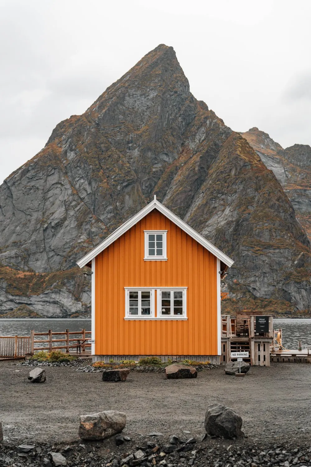 An ochre house with white windows in Sakrisøy in front of the pointed Olstind