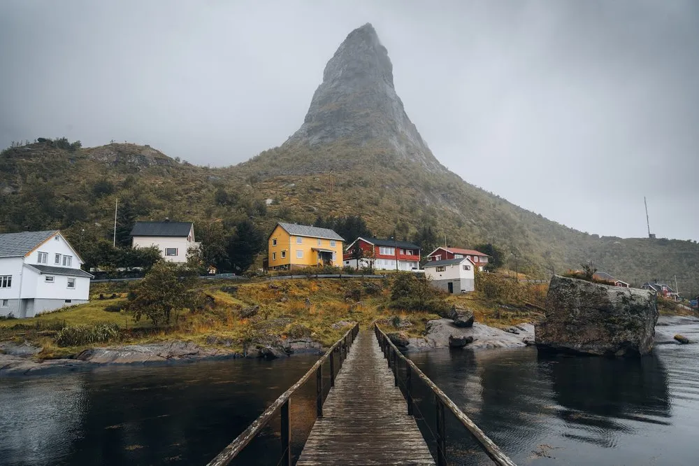 Von der Holzbrücke in Reine der Blick auf gelbe und rote Häuser und einen spitzen Berg im Dunst
