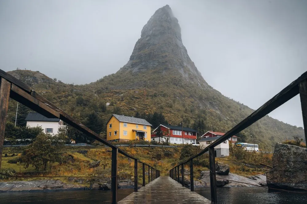 In Reine seen from a low angle over the wet wooden footbridge, a railing on either side, the pointed mountain behind